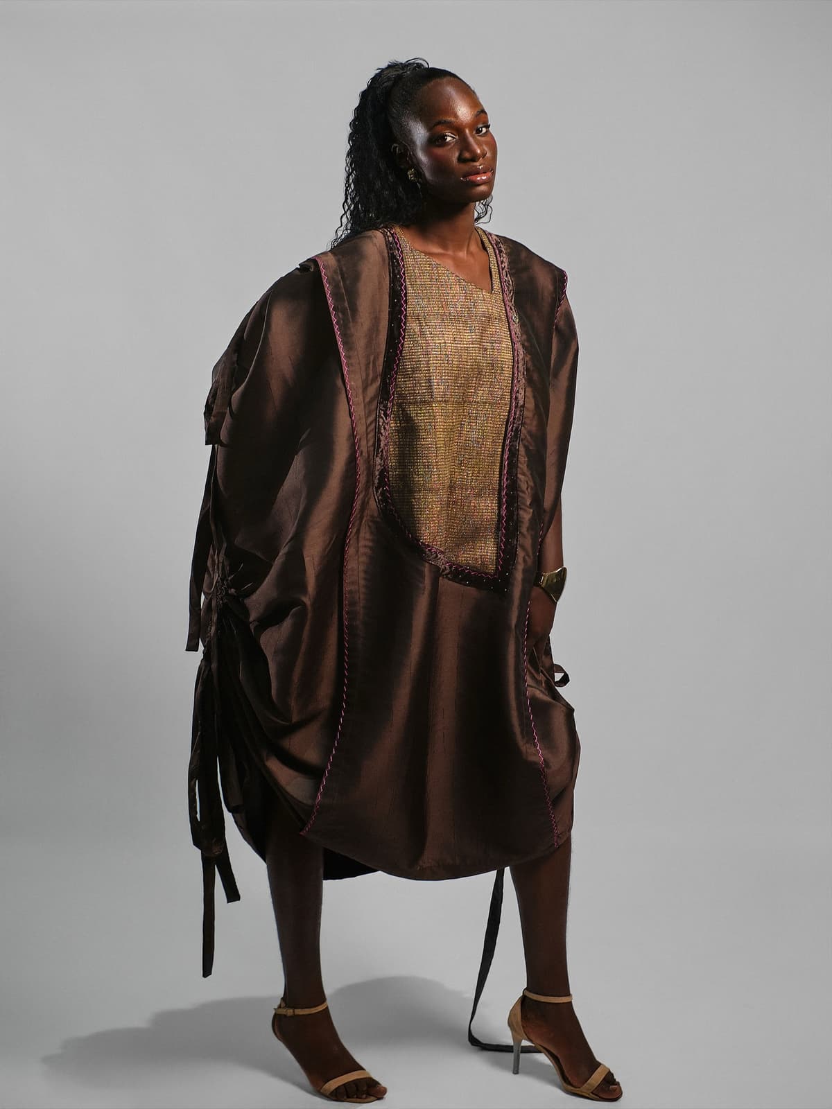 Cocoa satin cape-dress with a gold patterned bib and long tie straps.
